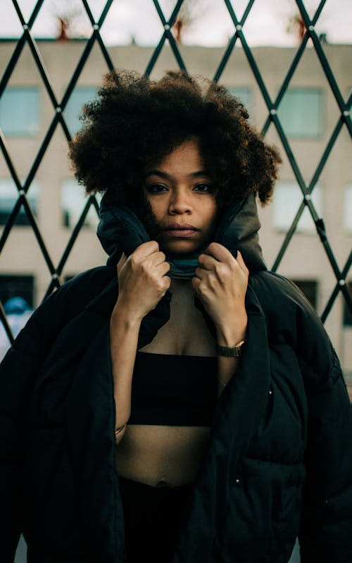 gratis Vrouw, Gekleed In Een Zwart Jasje Staat Voor Een Metalen Hek Stockfoto