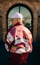 一位穿着五颜六色夹克和帽子的时尚男士站在城市的砖拱门前