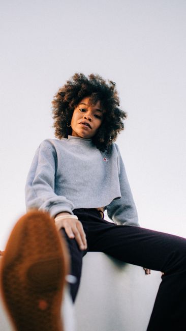 Portrait of a young black woman with natural hair sitting outdoors, showcasing fashion style.