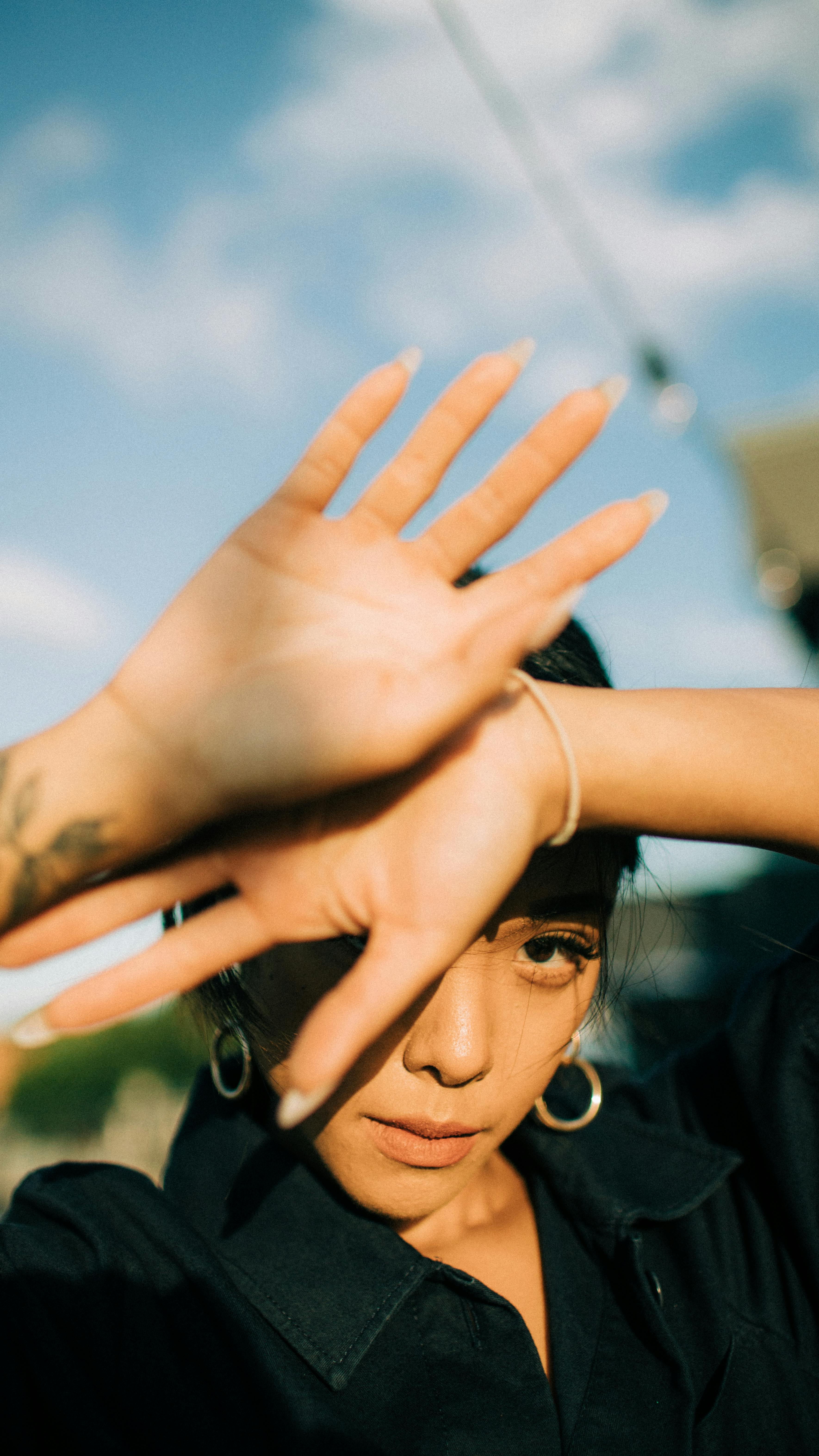 Young woman shielding her eyes from sunlight with her hands outside