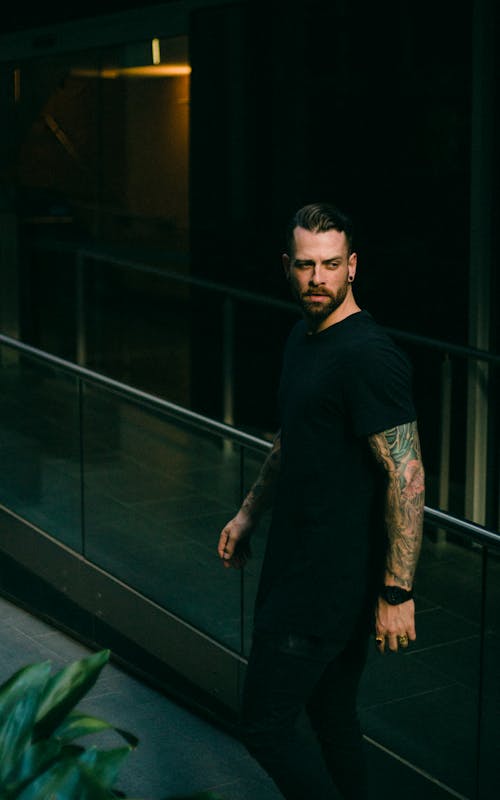 Free Man in Black Crew-neck Top With Arm Tattoos Looking Over His Shoulder Stock Photo