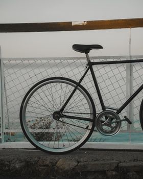 Stylish black bicycle resting against a fence overlooking a serene seascape at sunset.