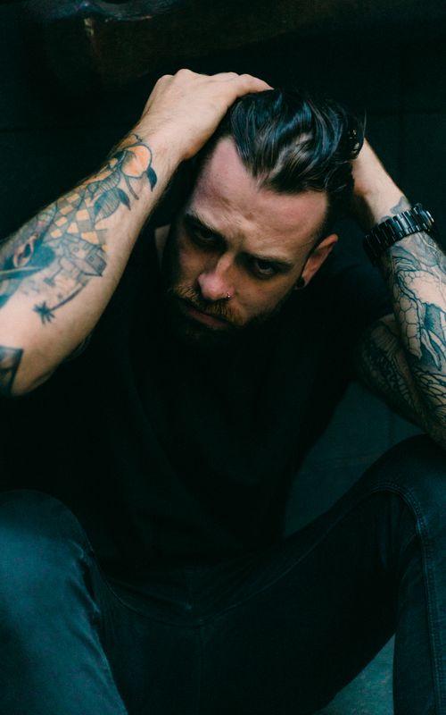 Free A thoughtful man with tattoos posing in a dark setting, exuding a moody, artistic vibe. Stock Photo