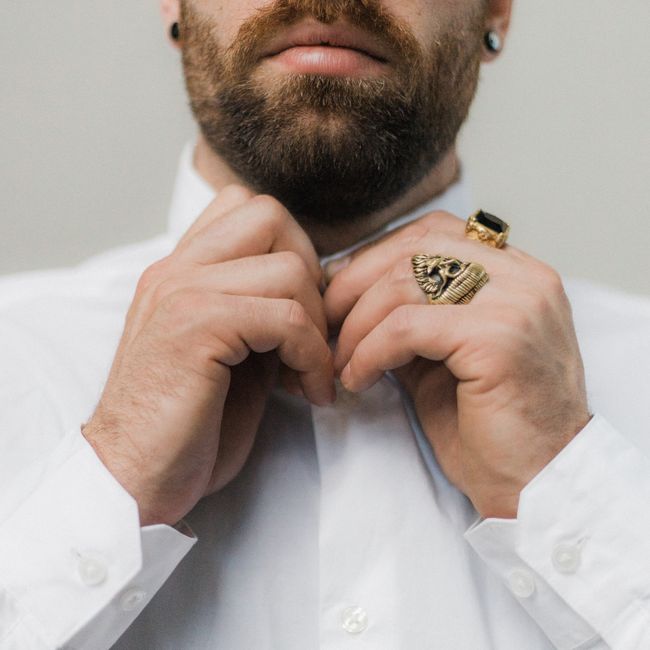 Close-up of a bearded man adjusting his shirt collar, showcasing stylish rings.