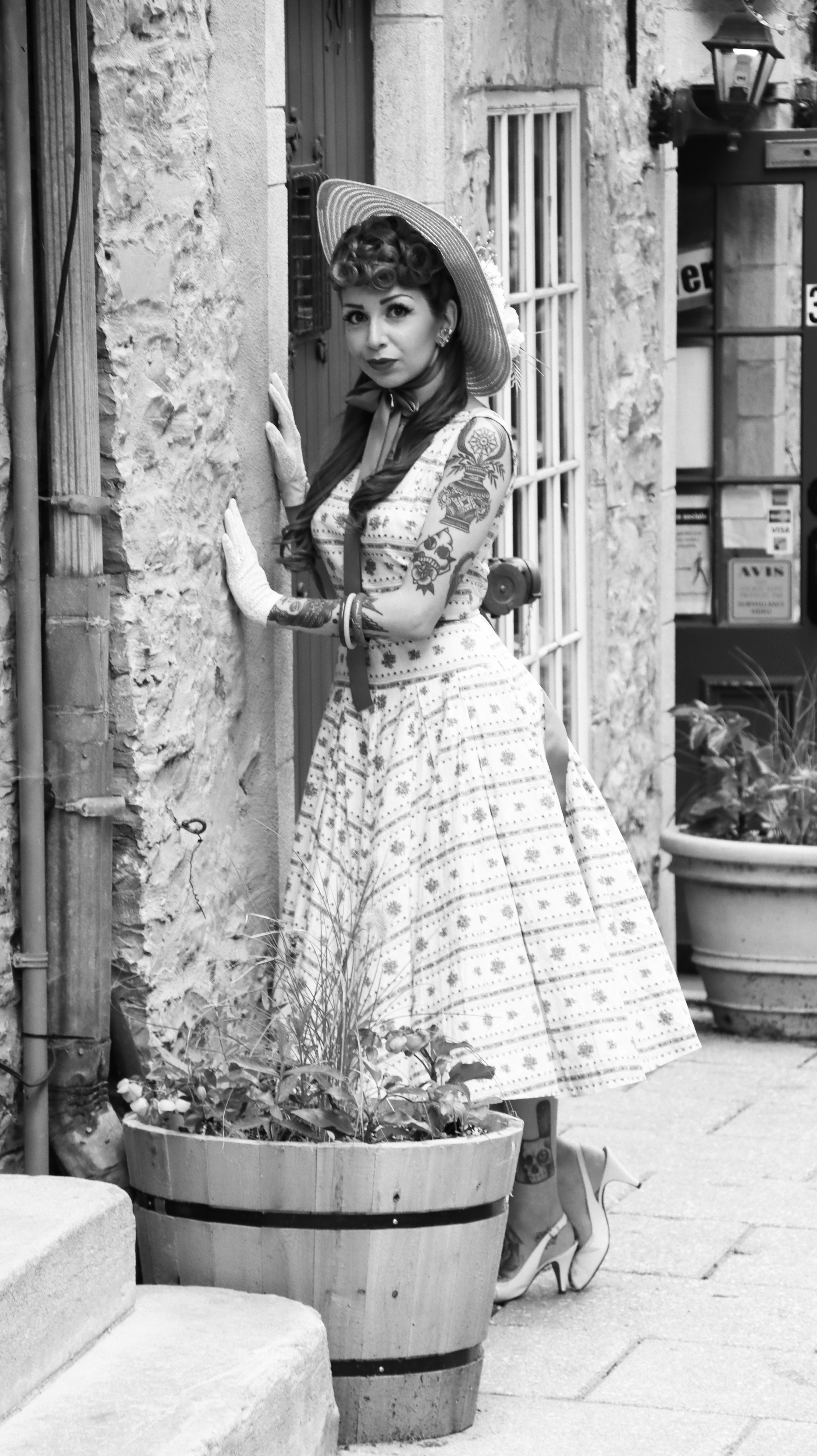 Black and white image of a vintage styled woman posing against rustic architecture.