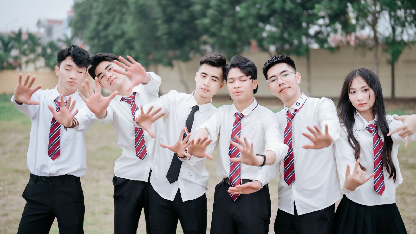 A group of teenagers in school uniforms posing outdoors with playful expressions.