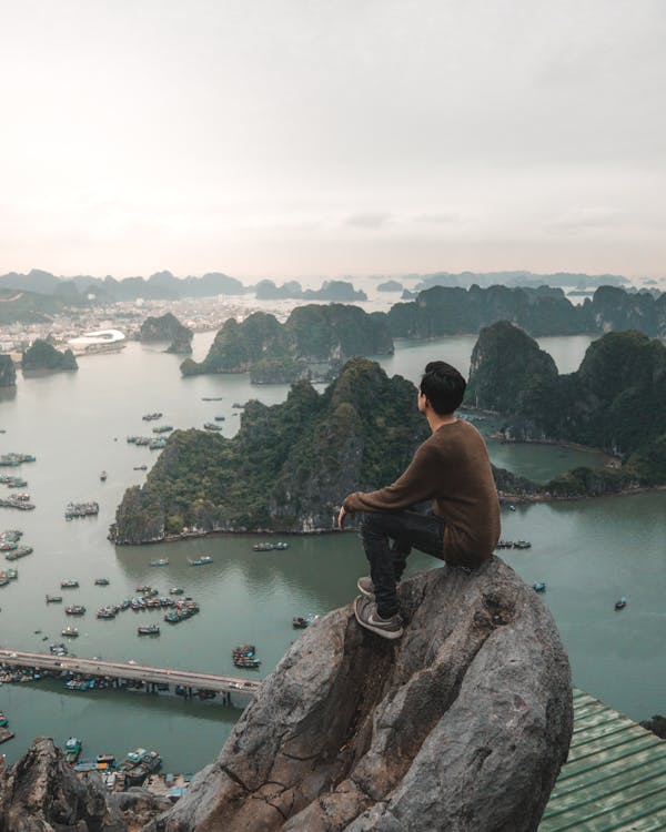 Free Man Sitting on Rock Overlooking the Famous Ha Long Bay in Vietnam Stock Photo