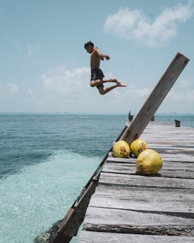 在墨西哥妇女岛，一名男子从木码头跃入清澈的海水，尽享阳光下的夏日乐趣