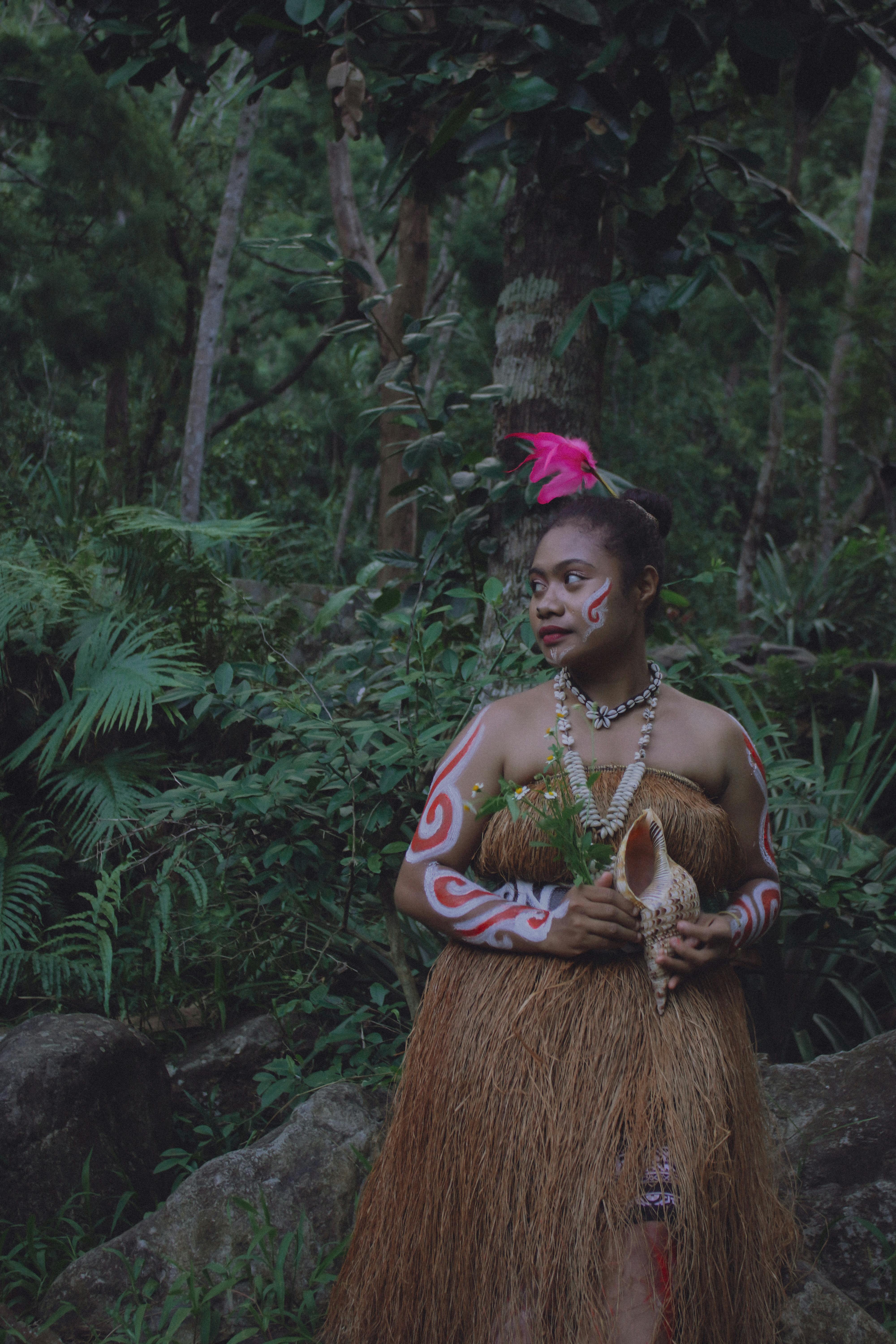 Indigenous woman wearing traditional attire with cultural body paint in a lush forest setting.