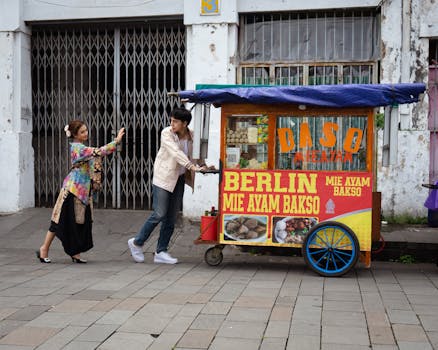 Street food vendors push a colorful food cart in Jakarta, showcasing local cuisine culture.