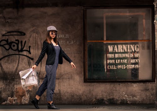 Photo of Woman Walking on Pavement While Holding Newspaper