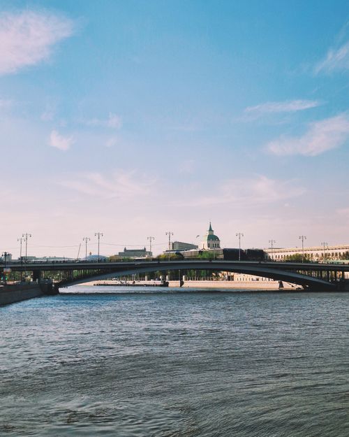 Free A picturesque scene of a bridge over a tranquil river with a historic building in the background. Stock Photo