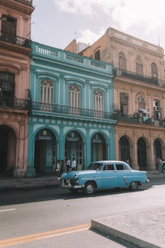 在古巴哈瓦那色彩缤纷的殖民建筑间，一辆经典古董汽车驶过