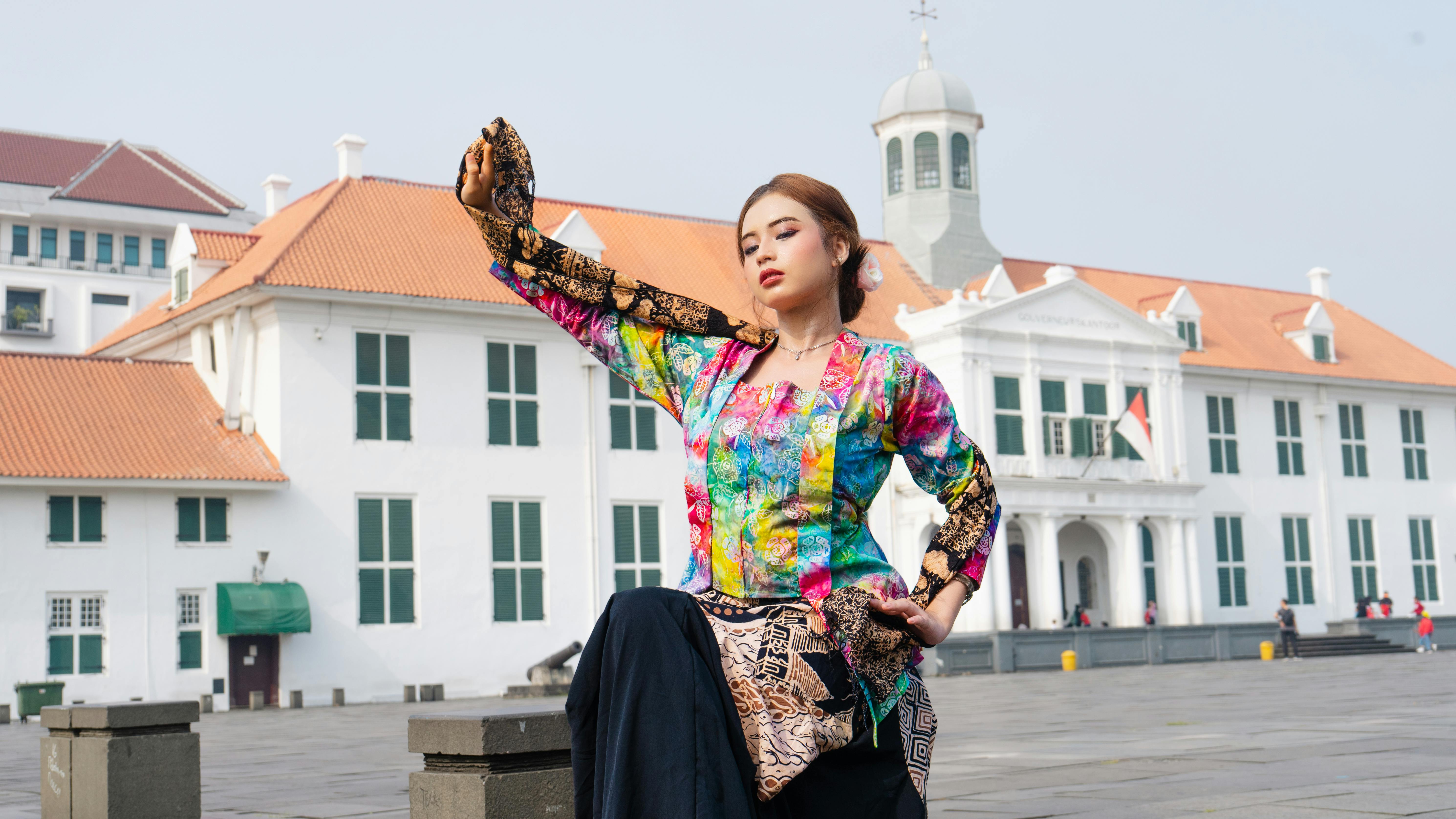 An Indonesian woman dances in traditional attire in front of a historic building in Jakarta, Indonesia. - Yakarta