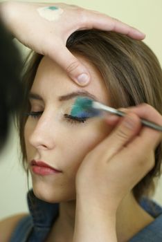Close-up of a makeup artist applying vibrant eyeshadow to a woman's eyelid.