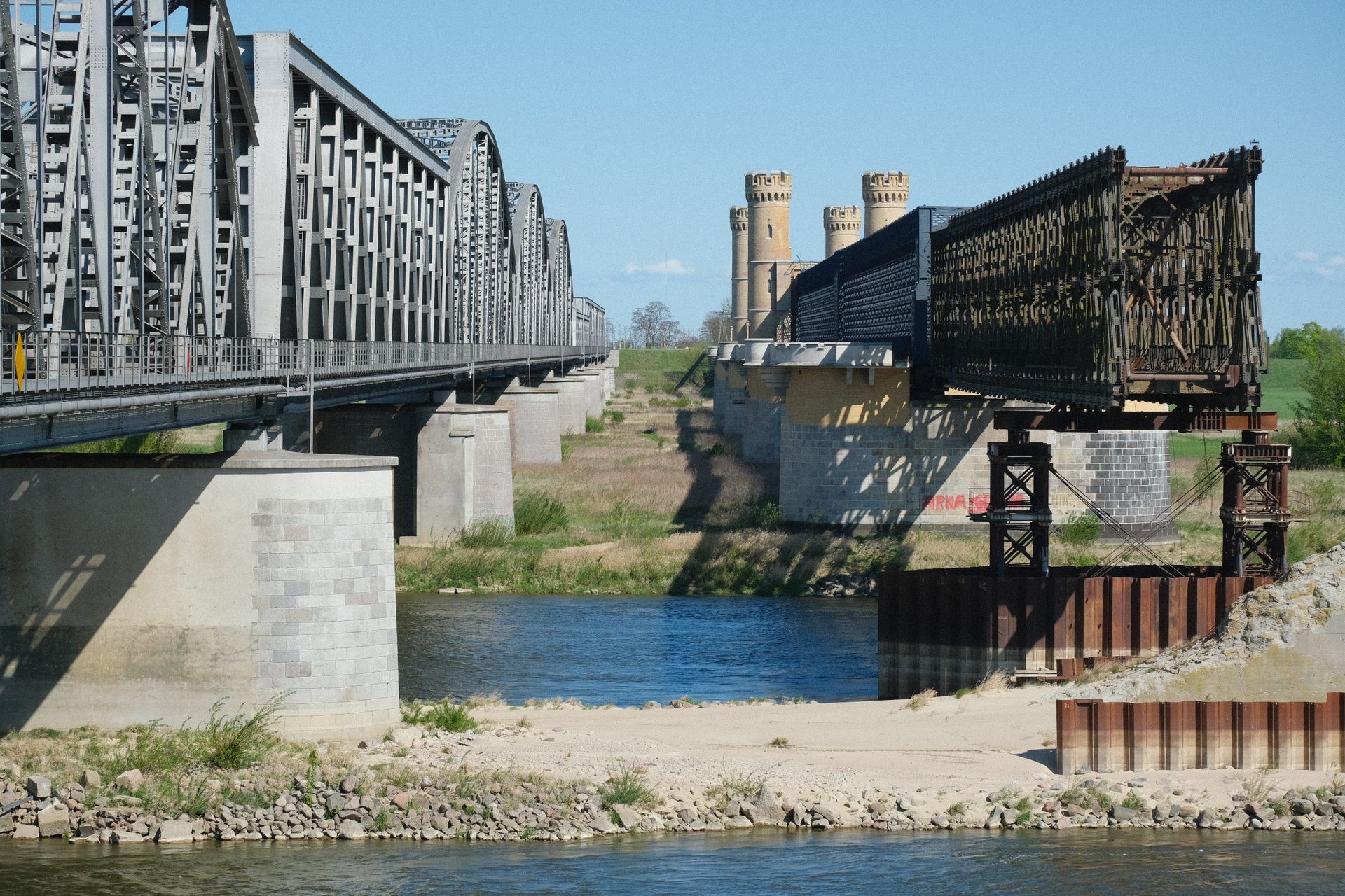 View of two parallel iron bridges spanning over a calm river on a sunny day.