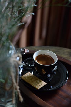 Close-up of an espresso cup with a biscuit on a wooden tray, offering a cozy autumn vibe.