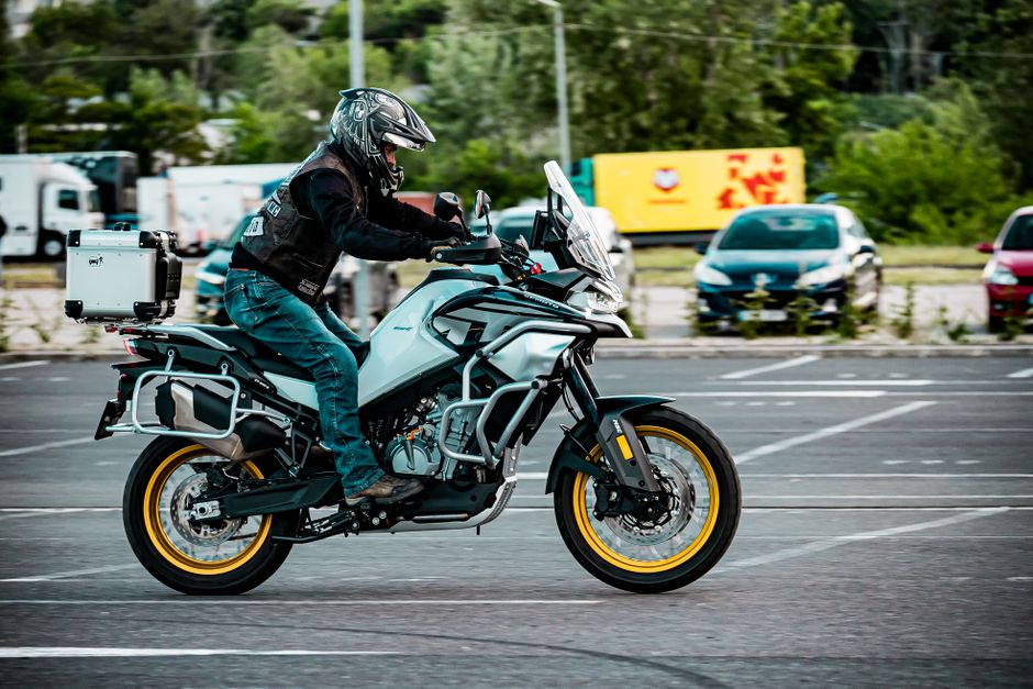 A motorcyclist rides an adventure touring motorcycle in an open parking area. Outdoor action shot.
