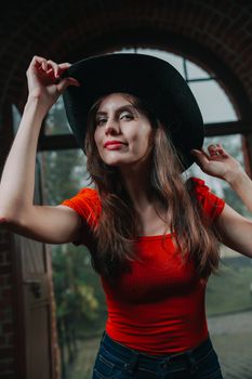 Portrait of a woman in a black hat and red top posing confidently indoors.