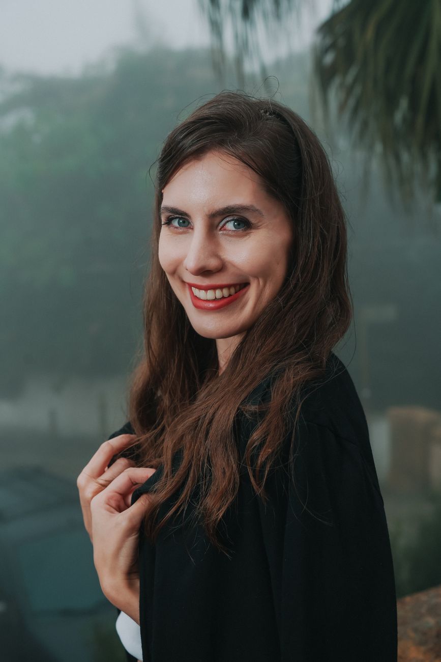 A woman with long brown hair smiles warmly, outdoors on a misty day.