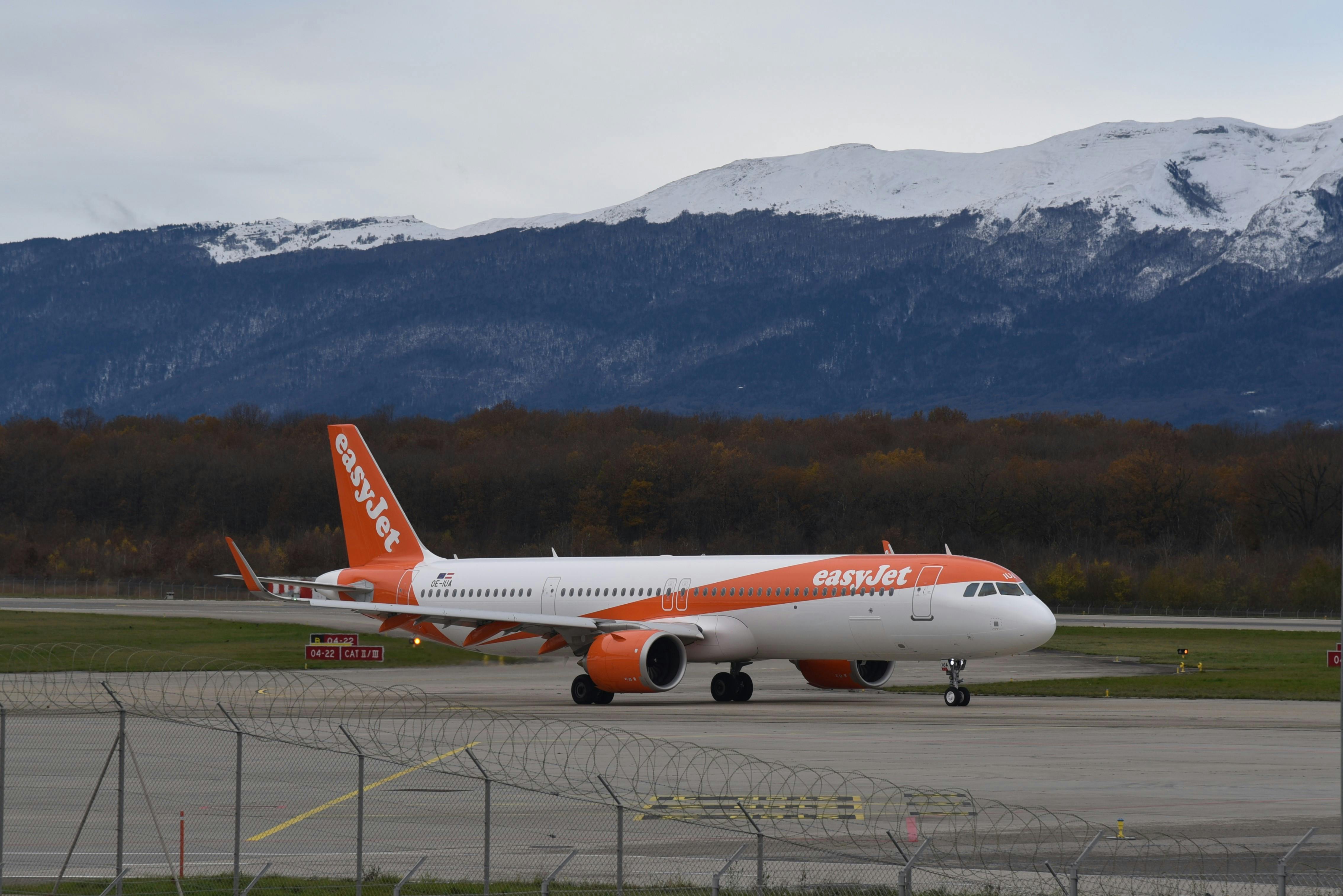 EasyJet Airbus A321 taxiing at Geneva Airport with scenic mountain backdrop.