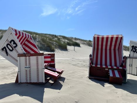 Cozy red and white beach chairs on pristine sandy dunes under clear blue sky.