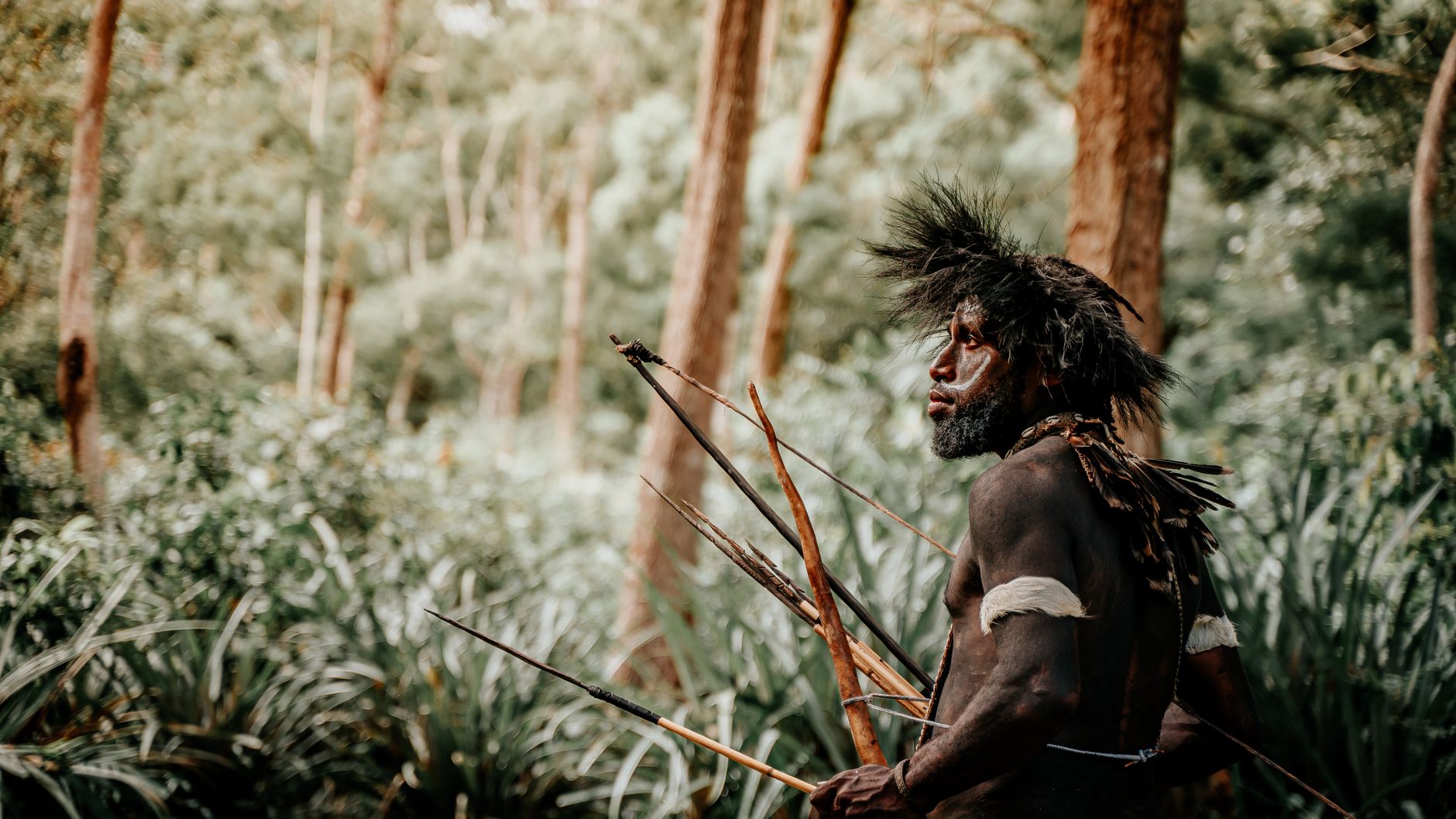 Traditional tribal hunter in forest with spears and headdress.