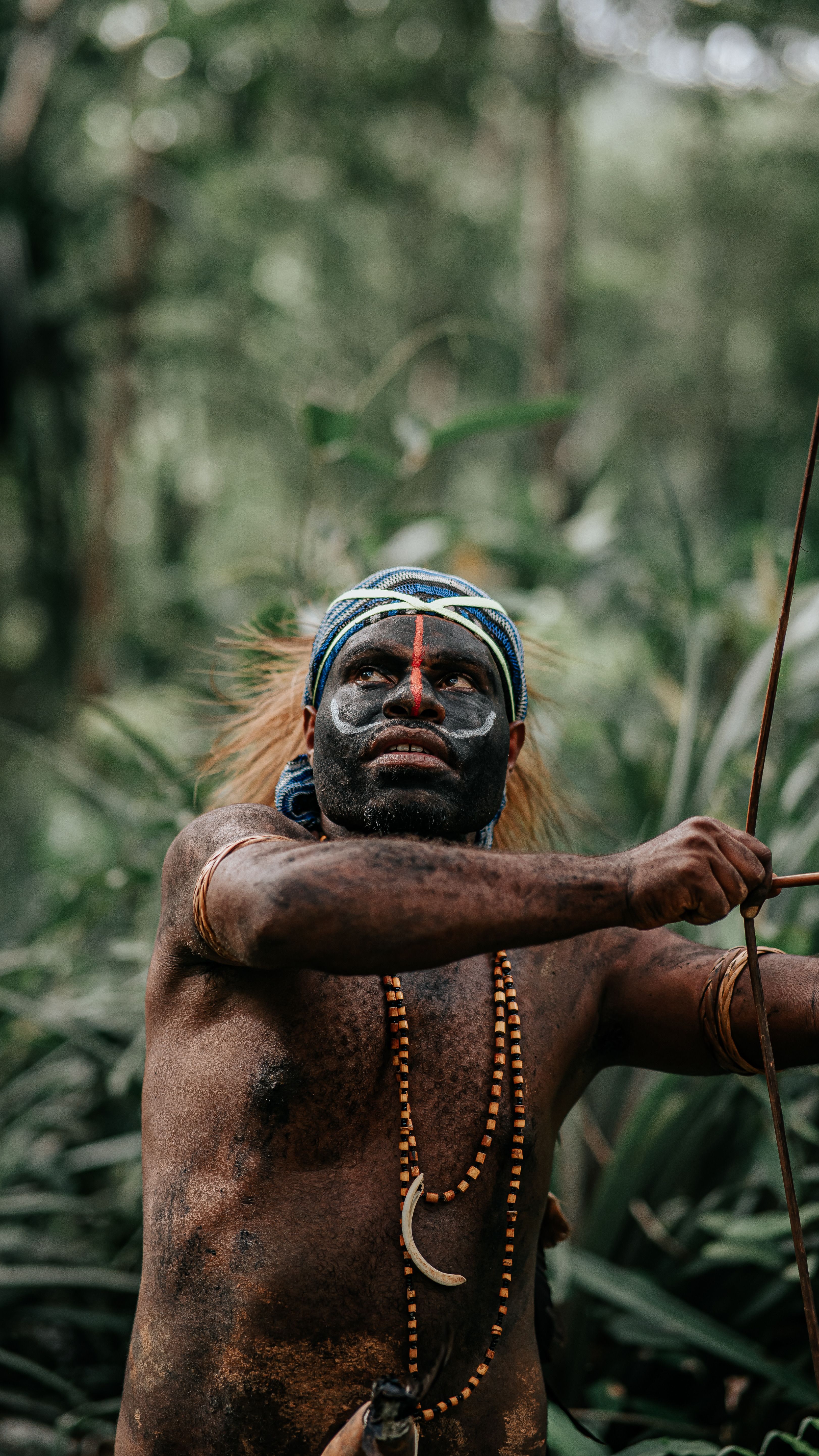 Indigenous man with traditional face paint holding a bow in a lush jungle setting.