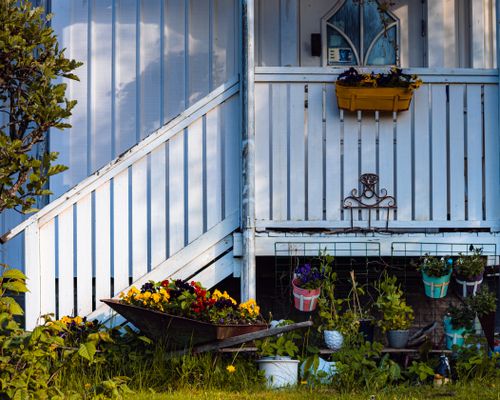 Free A rustic porch adorned with colorful flower pots and a charming wheelbarrow display. Stock Photo
