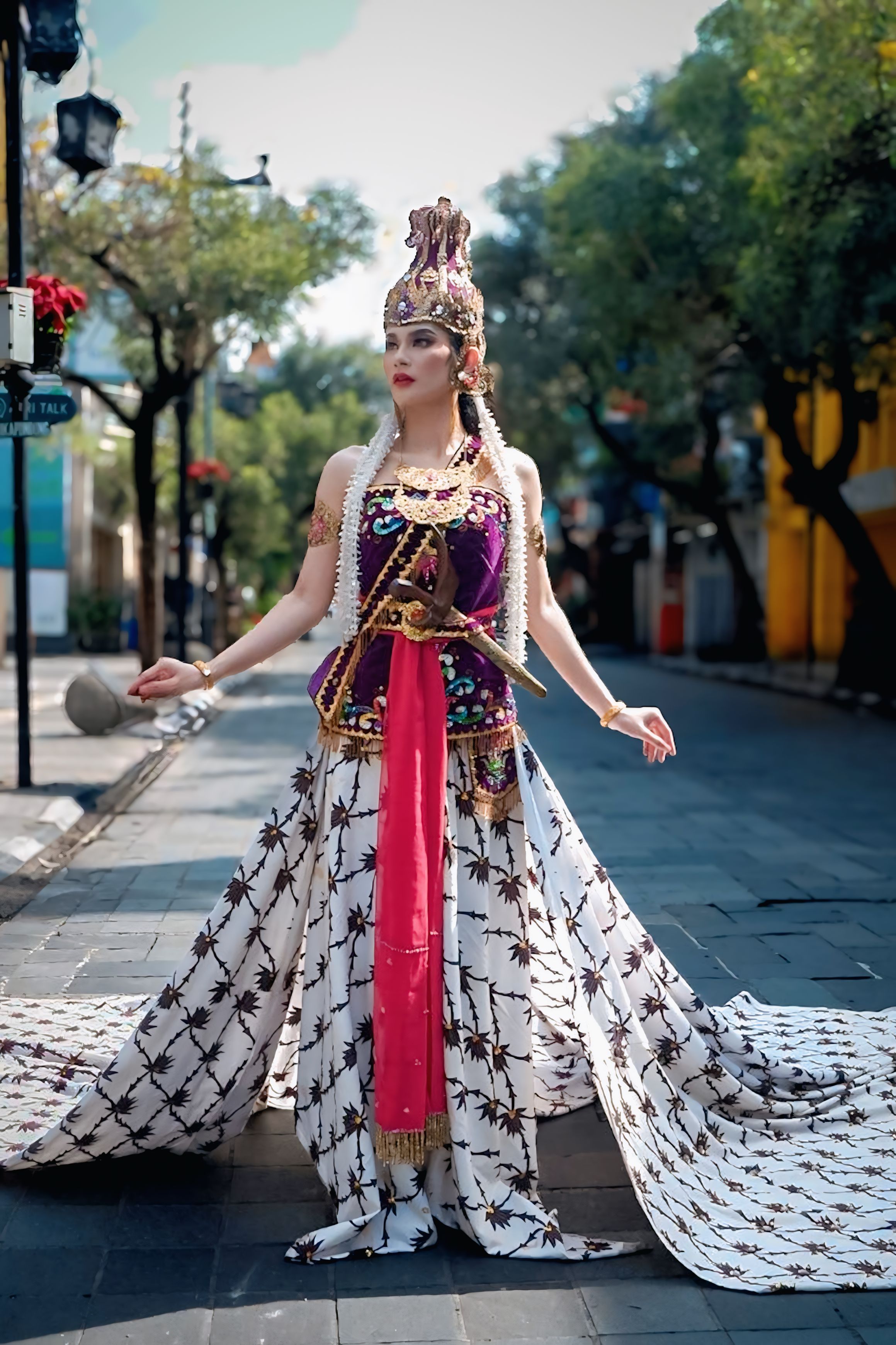 Elegantly dressed woman in Javanese costume poses gracefully on a city street.