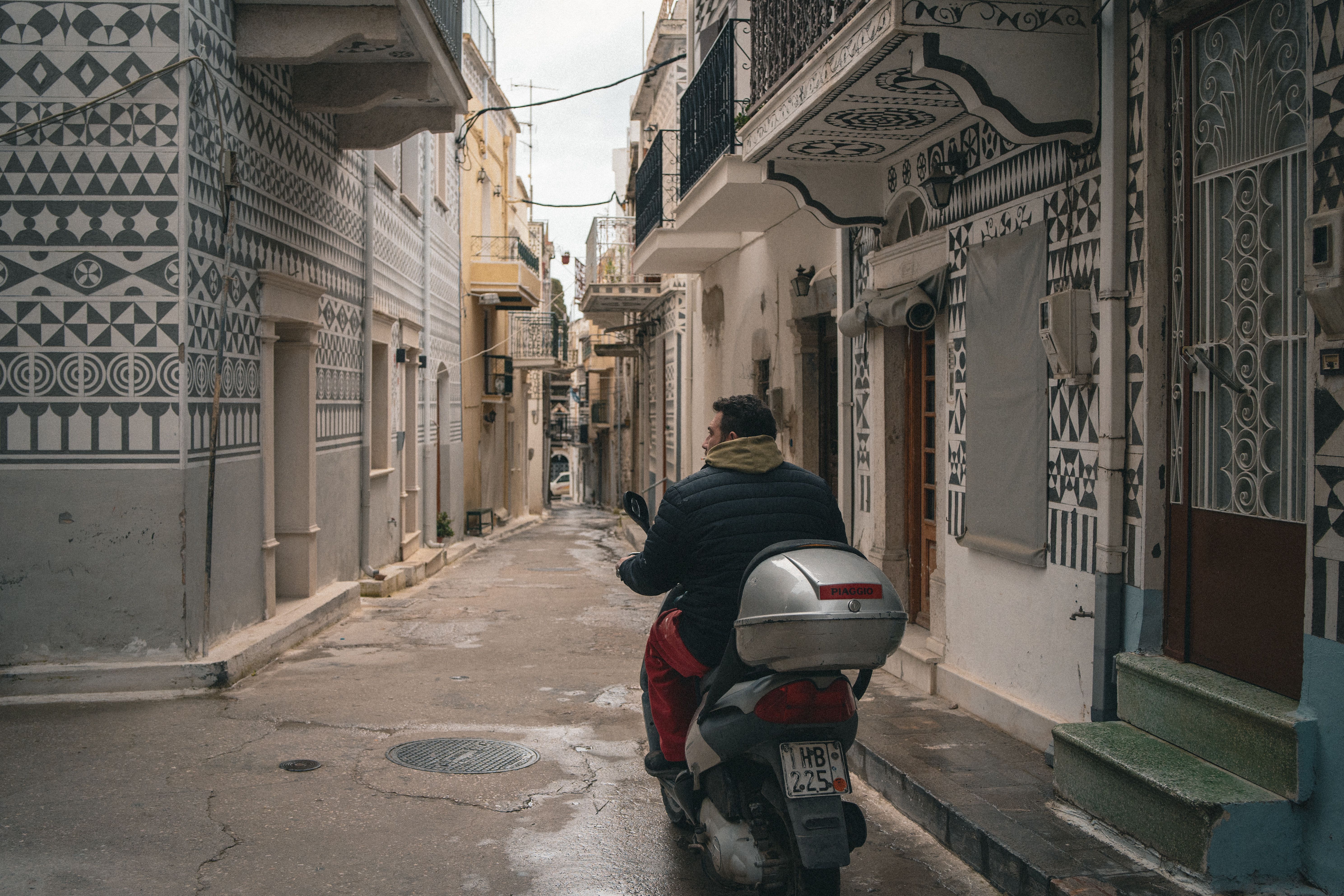 A man riding a scooter through a narrow alleyway in a traditional village with decorative facades.