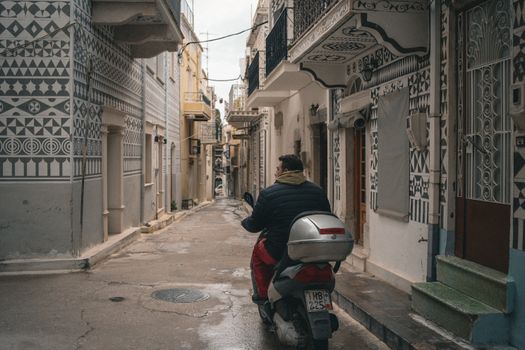 A man riding a scooter through a narrow alleyway in a traditional village with decorative facades.