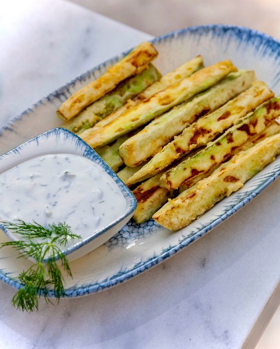 Golden egg-battered zucchini sticks on a blue-rimmed platter with a bowl of dill yogurt sauce