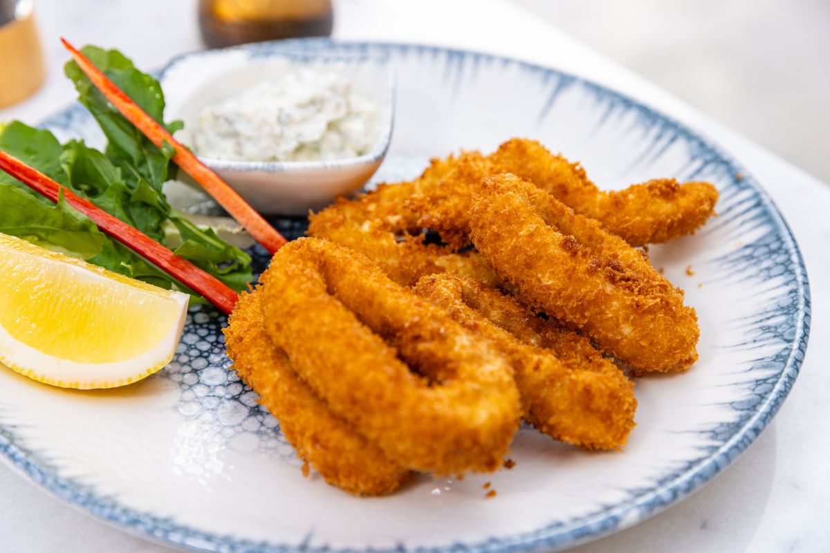 Calamari fritti dorati serviti su un piatto decorato di blu, con spicchio di limone