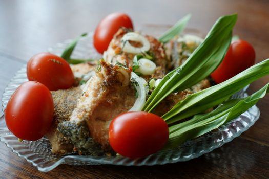 Mouth-watering fried fish served with tomatoes, onions, and green leaves on a glass plate.