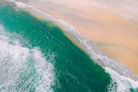 这张航拍照片令人惊叹，碧绿的海浪拍打着宁静的沙滩，尽显大自然的美丽