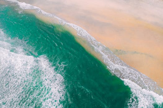 这张航拍照片令人惊叹，碧绿的海浪拍打着宁静的沙滩，尽显大自然的美丽