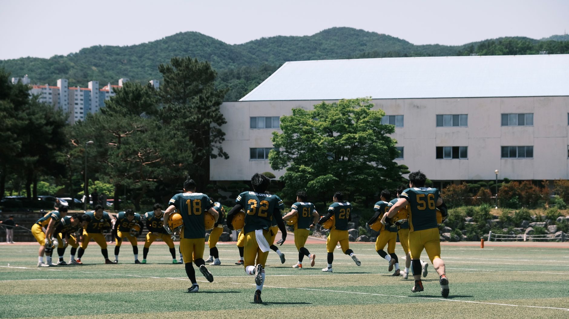 Football team in uniform practicing outdoors with mountains in background on a sunny day.