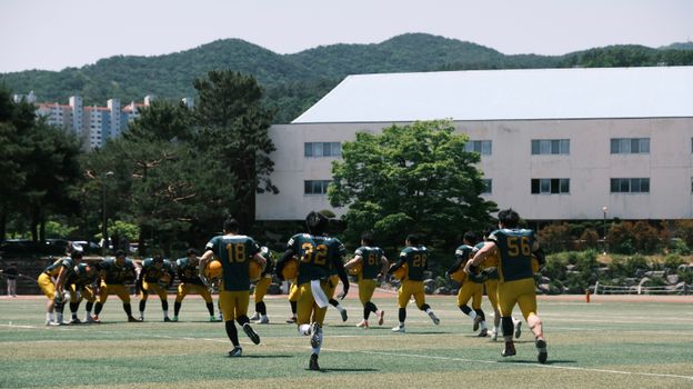 Football team in uniform practicing outdoors with mountains in background on a sunny day.