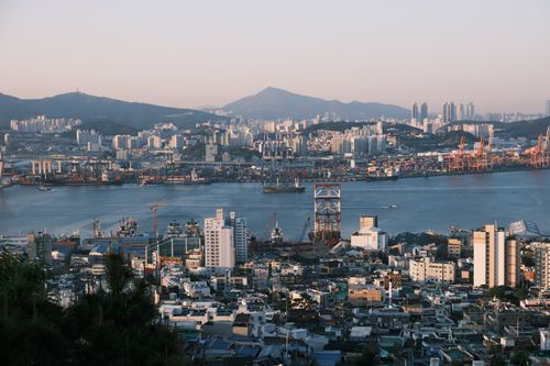 Free Stunning view of a bustling port city at sunrise with cranes, buildings, and mountains. Stock Photo