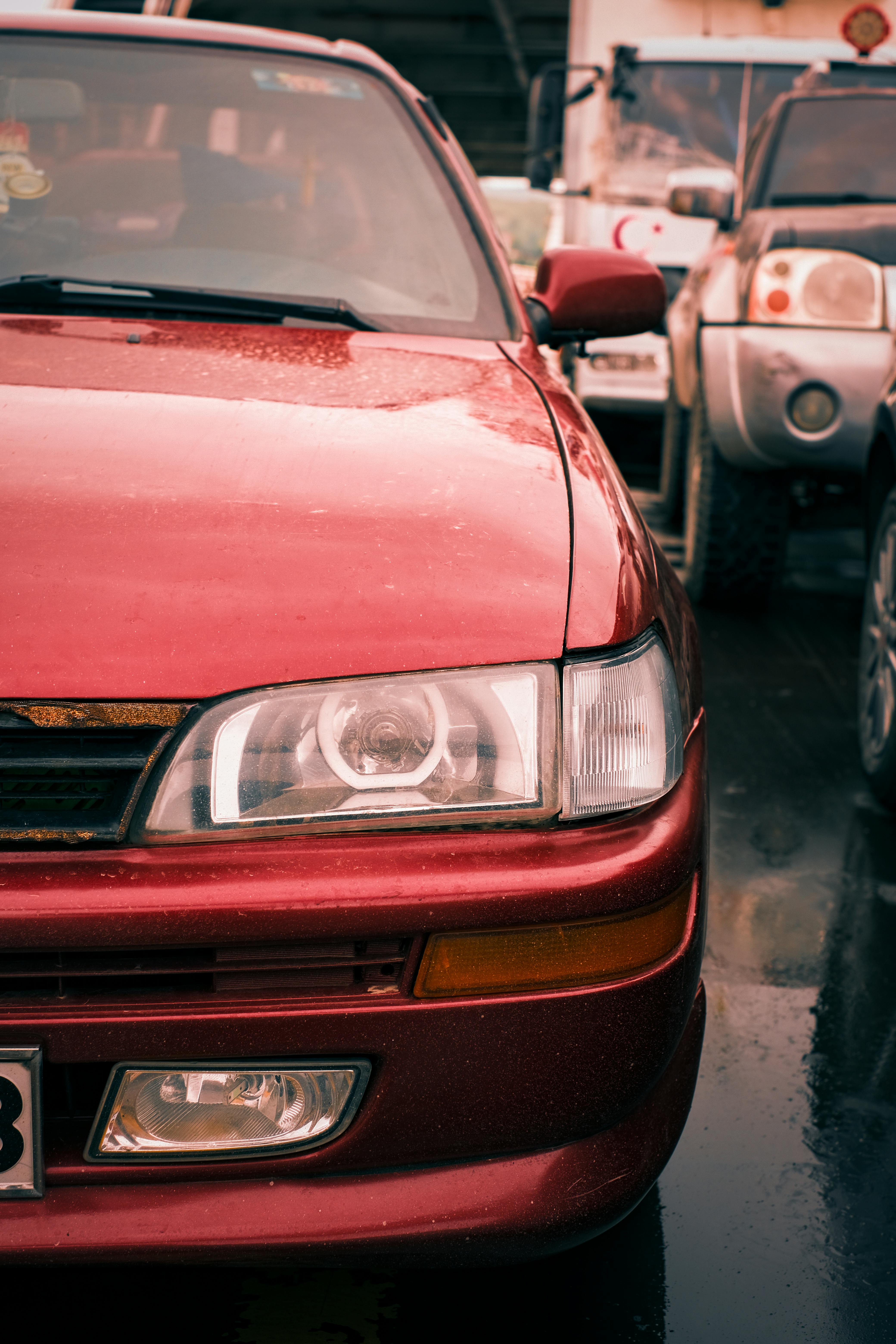 Classic red car front view with headlight detail in rainy weather, showcasing vintage automotive style.