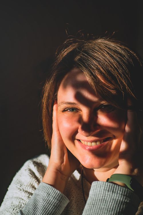 Free A woman smiling warmly with sunlight casting shadows across her face and hands. Stock Photo