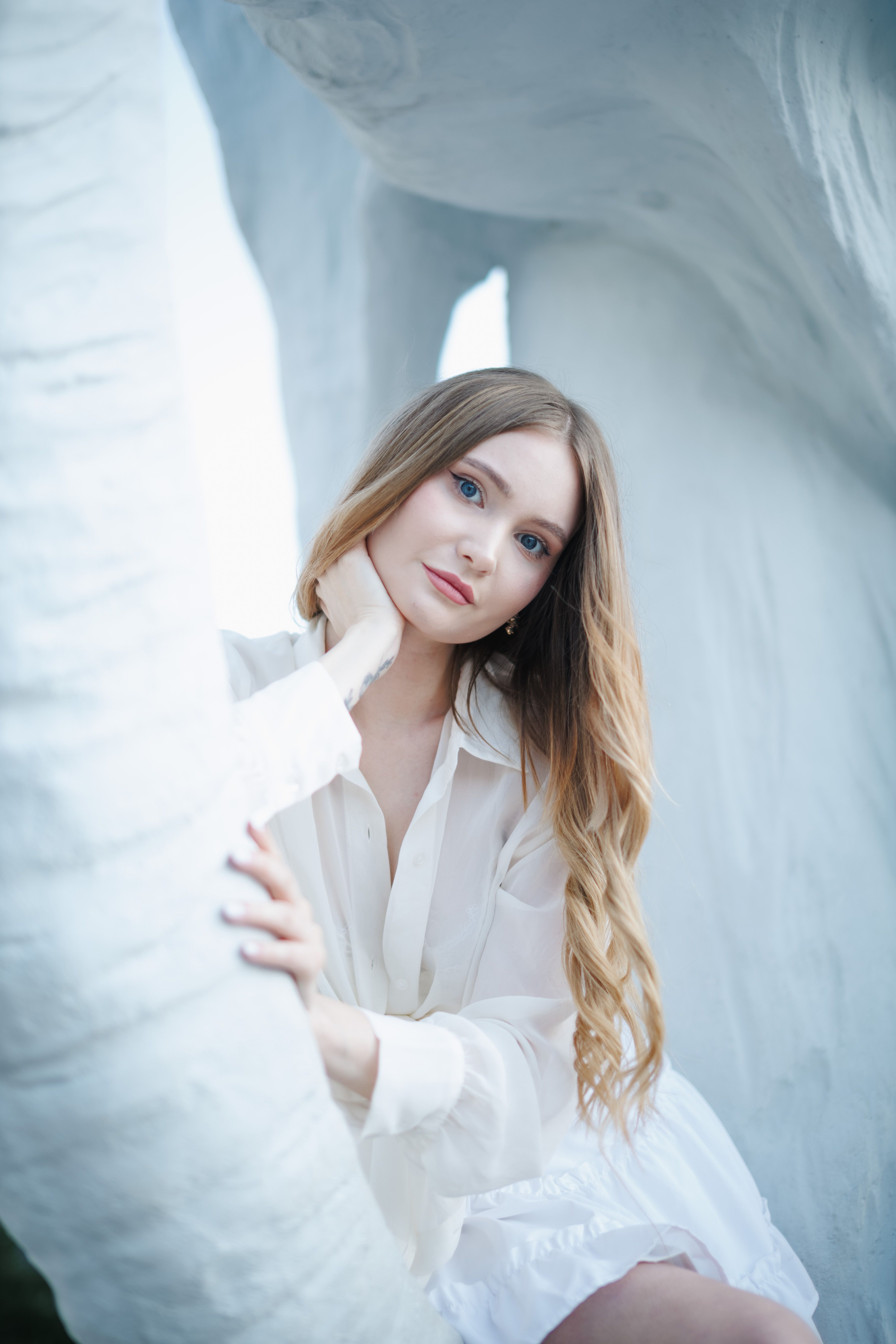 A serene portrait of a woman with flowing blonde hair, set against a minimalist white background.