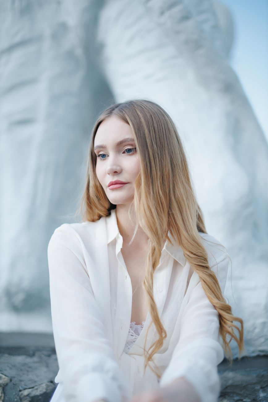 A serene woman in white poses in front of a large monument, exuding calm elegance.