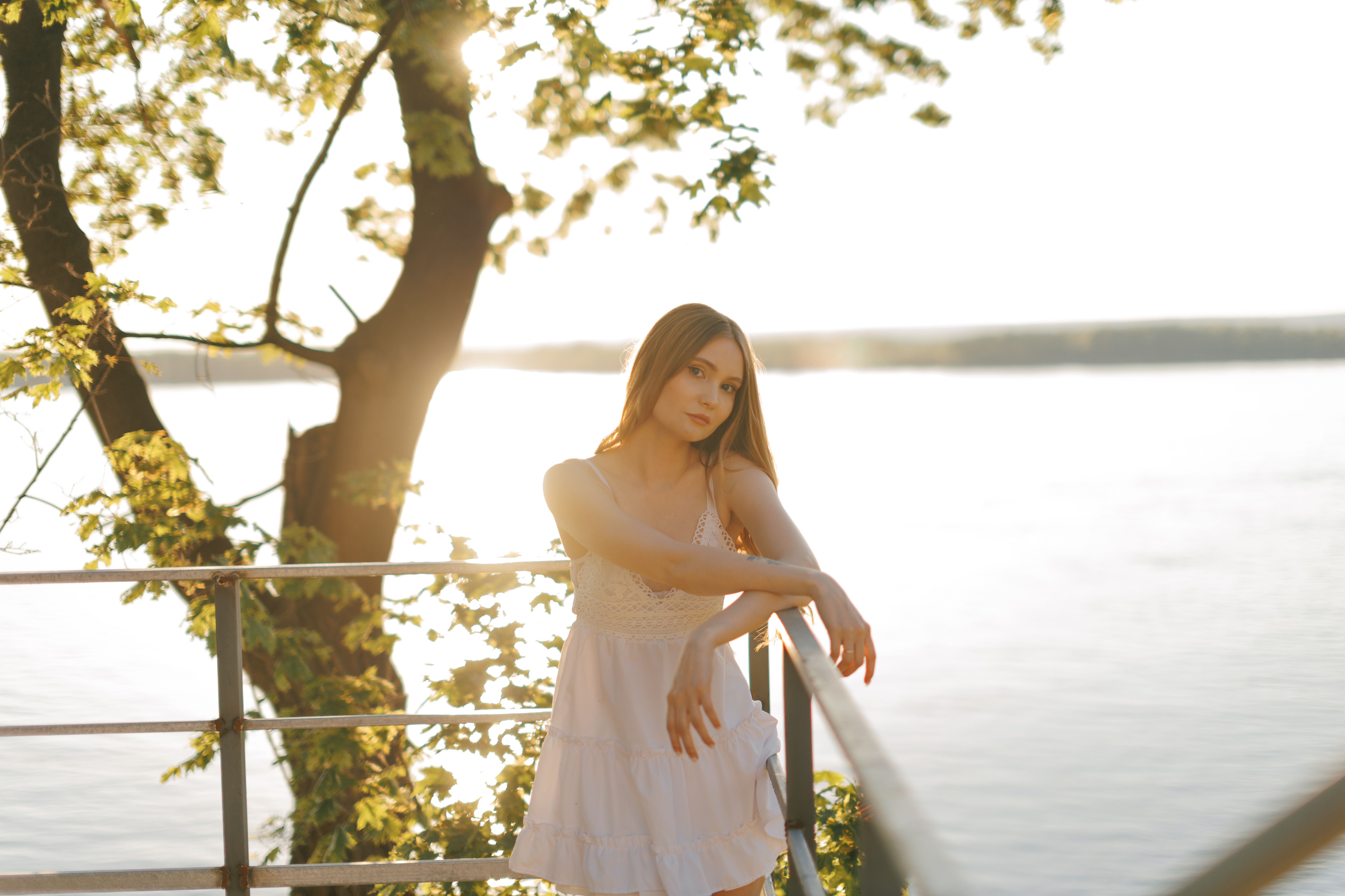 Young Woman Relaxing by Lakeside Railing at Sunset · Free Stock Photo