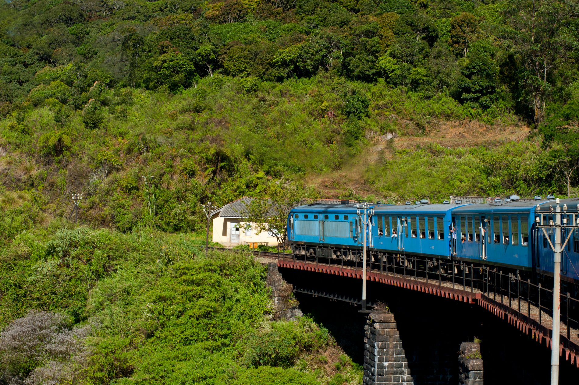 A blue train passing through the green hills around Ella, Sri Lanka