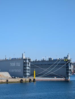 Industrial ship anchored at port under clear blue sky, cables secured to dock.