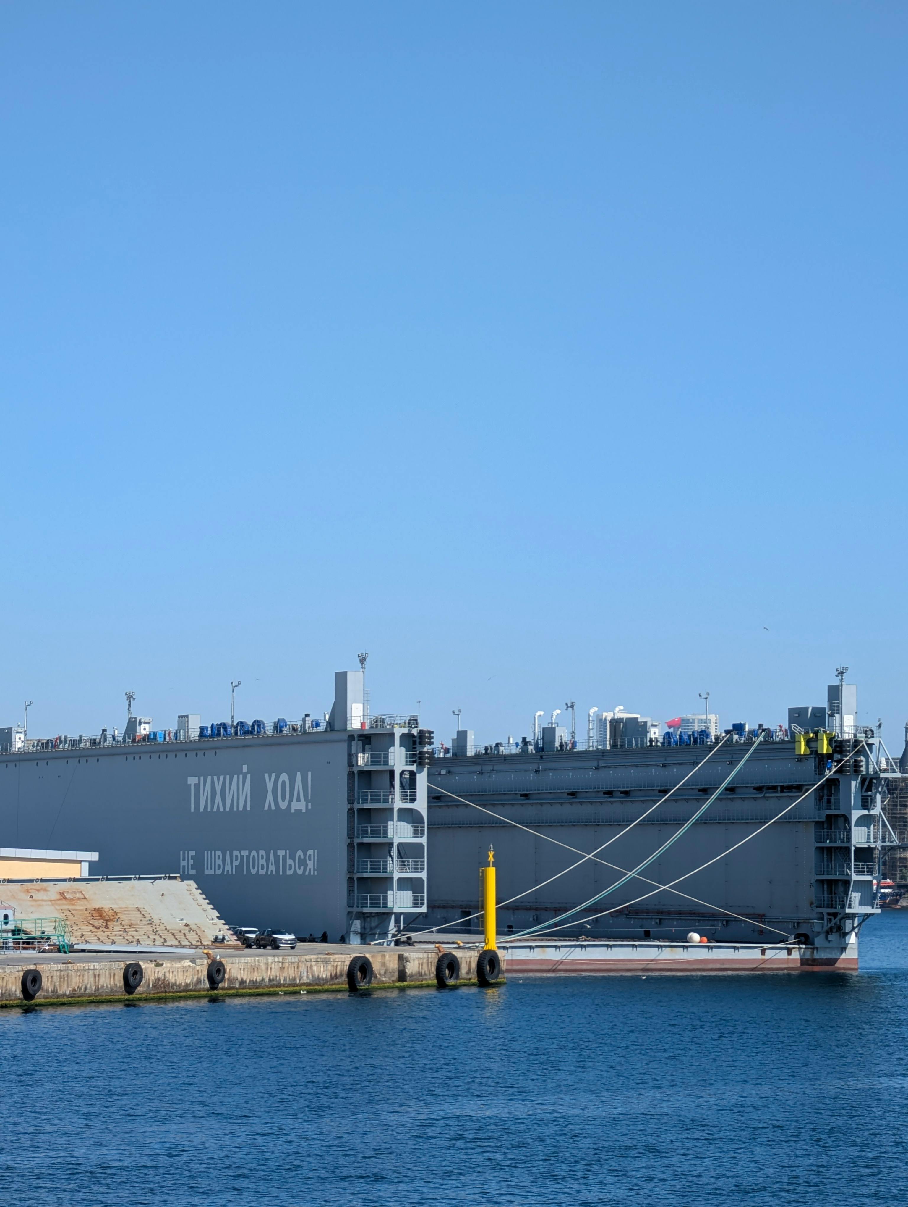 Gratuit Un grand navire industriel amarré dans un port sous un ciel bleu clair, avec un texte visible en cyrillique. Photos