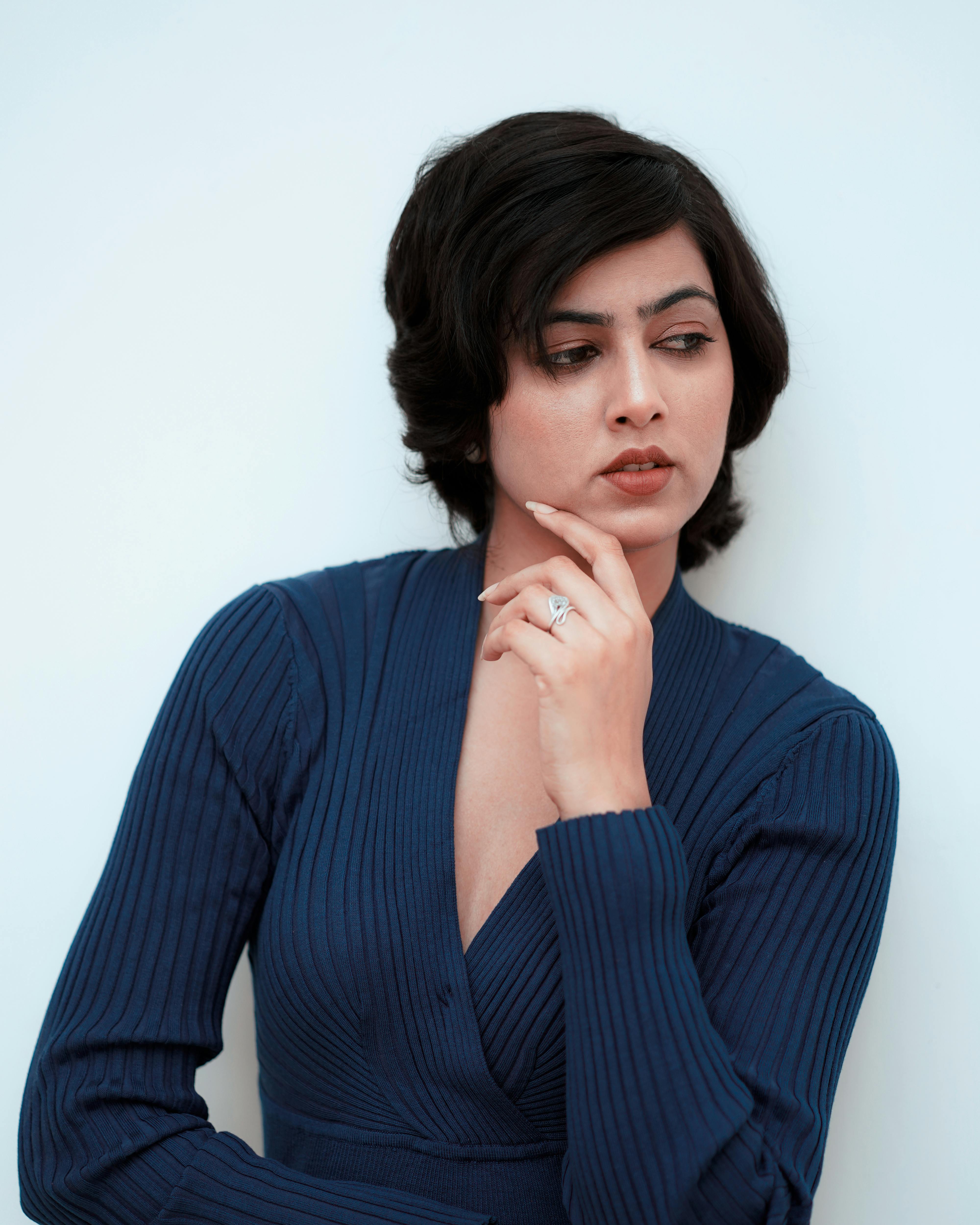 Sophisticated woman in a blue knitted dress posing thoughtfully against a neutral background.