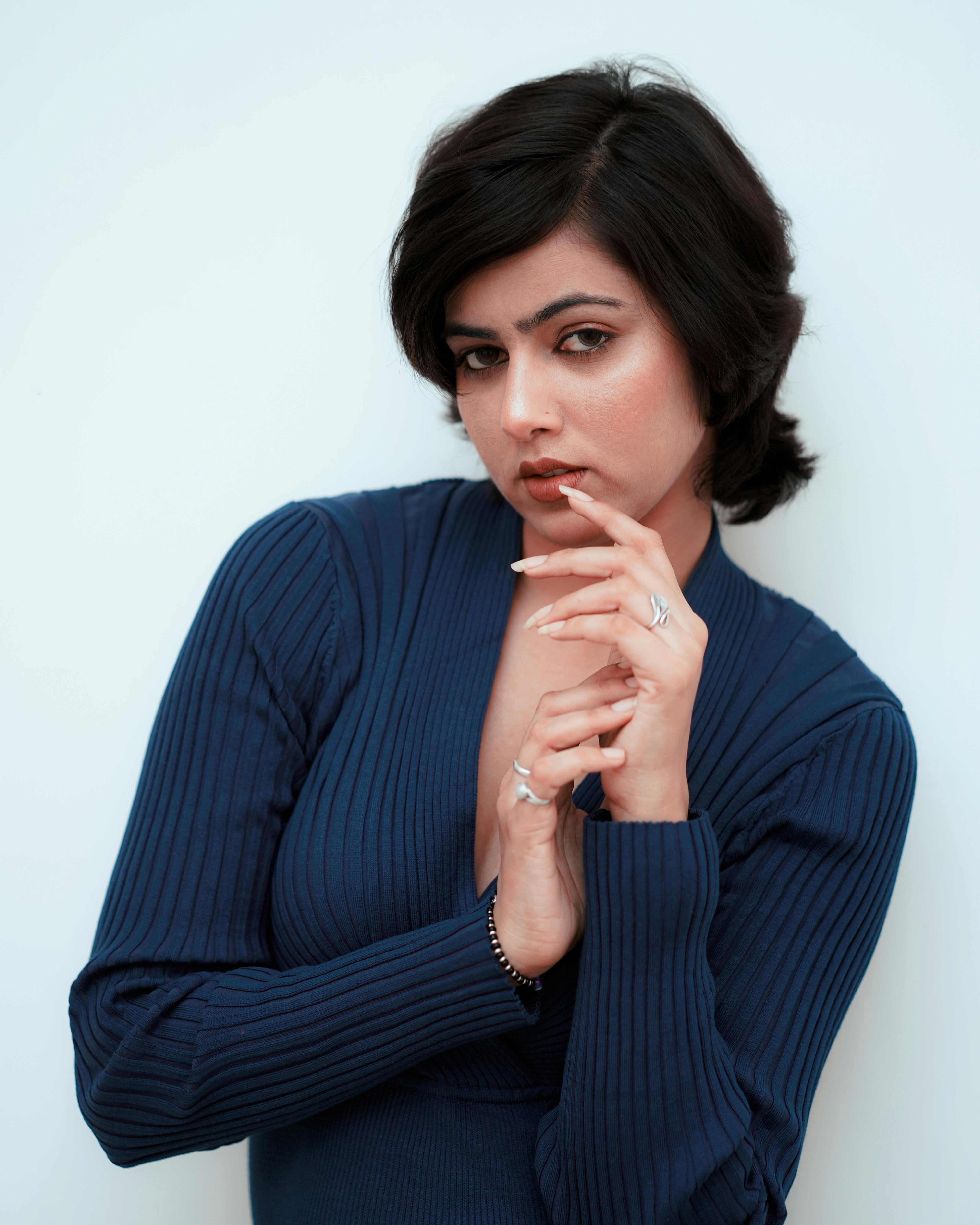 Close-up portrait of a woman in a blue sweater posing with confidence against a light background.